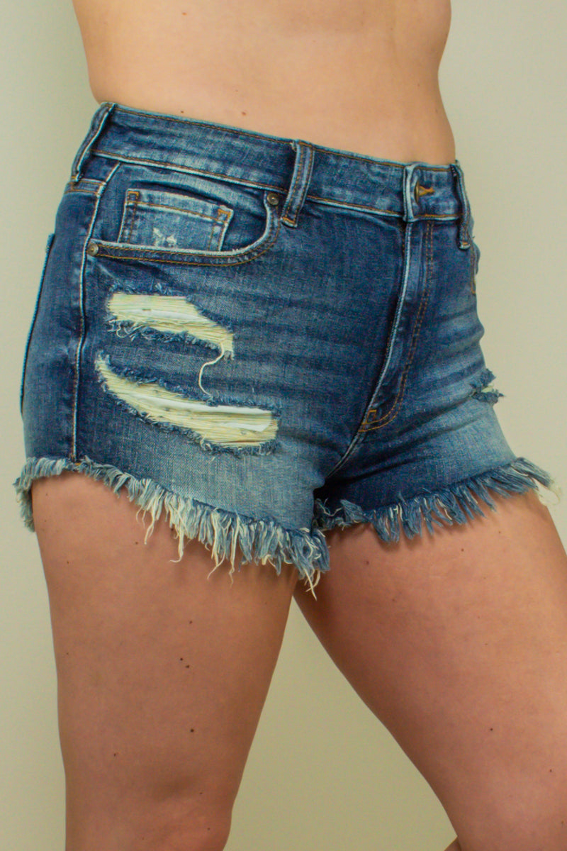 high waisted dark wash distressed denim shorts with frayed ends, side view